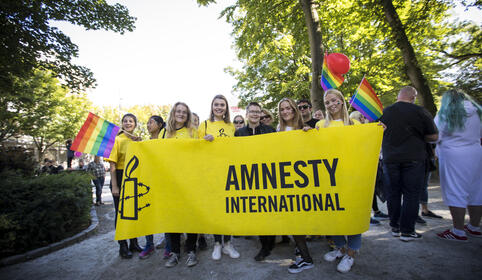 Ungdommer p&aring; Pride st&aring;r bak et Amnesty-banner og smiler til kamera. 
