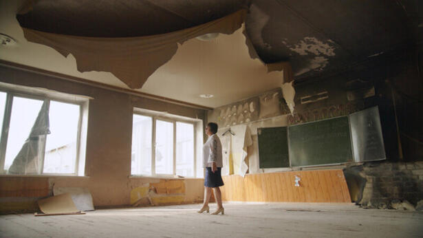 Kvinne st&aring;r midt i et klasserom &oslash;delagt etter russiske angrep