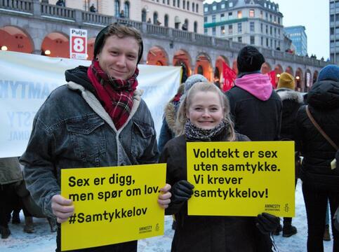 Mann og kvinne st&aring;r med plakater under 8. mars-markering. Plakatene sier "Sex er digg, men sp&oslash;r om lov. Samtykkelov n&aring;!"