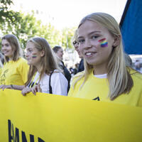 Ungdommer p&aring; Pride st&aring;r bak et Amnesty-banner og smiler til kamera. 
